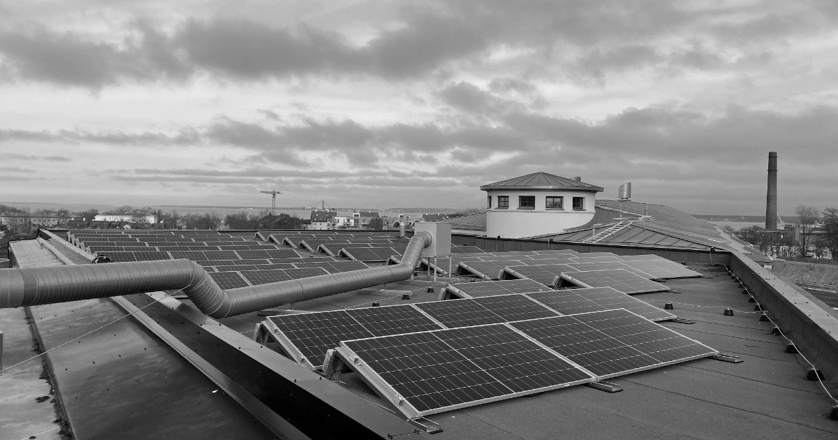 Painéis solares instalados no telhado plano de um edifício, sob céu nublado, em preto e branco
