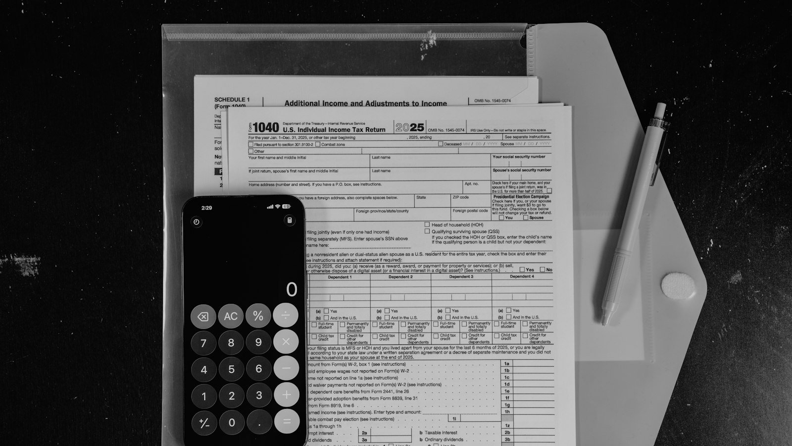 Calculadora e caneta sobre formulários de imposto impressos, em preto e branco